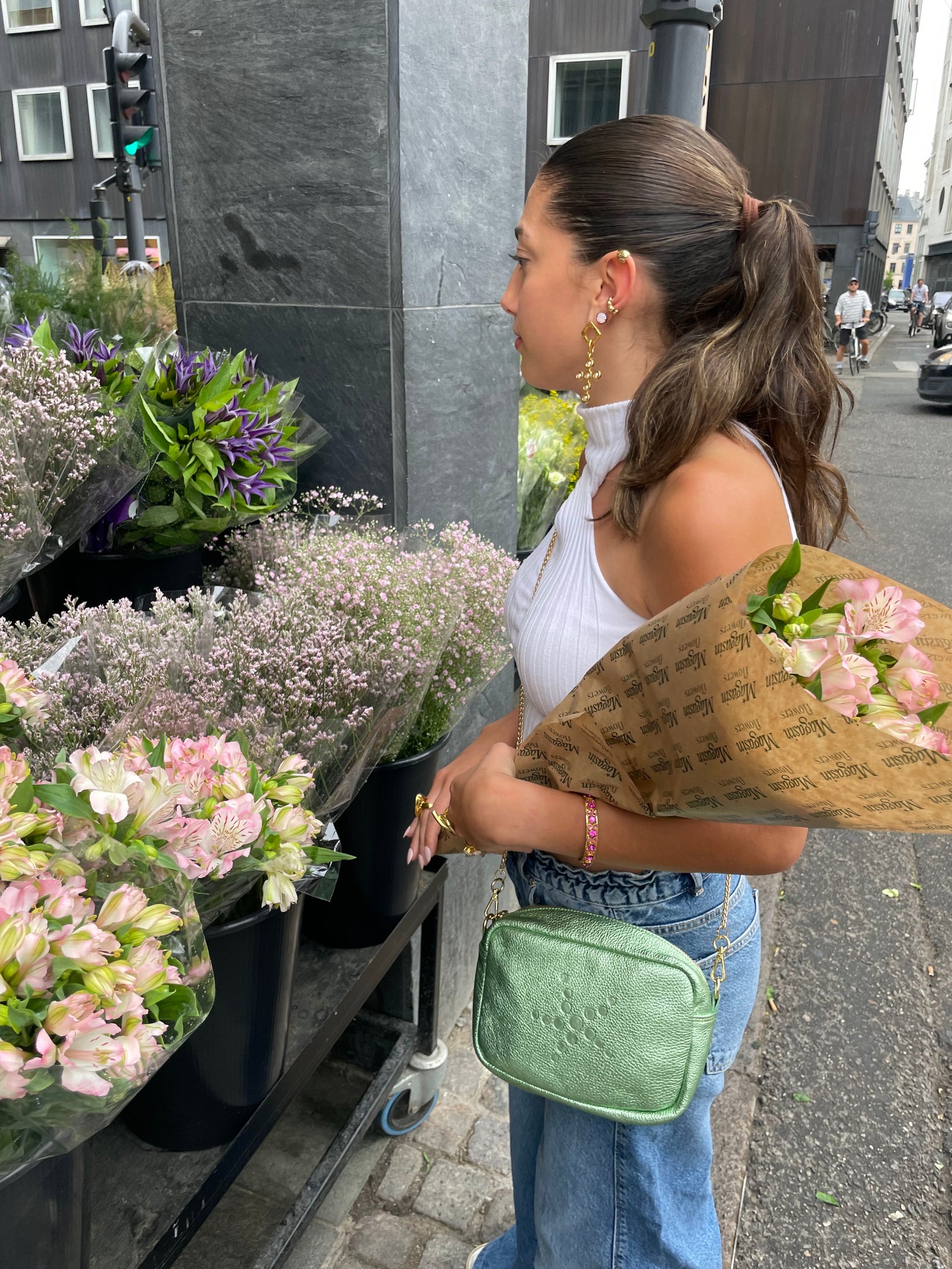 Woman holding a bouquet of flowers on a street, and Green Metallic Gabriela with flower stands in the background