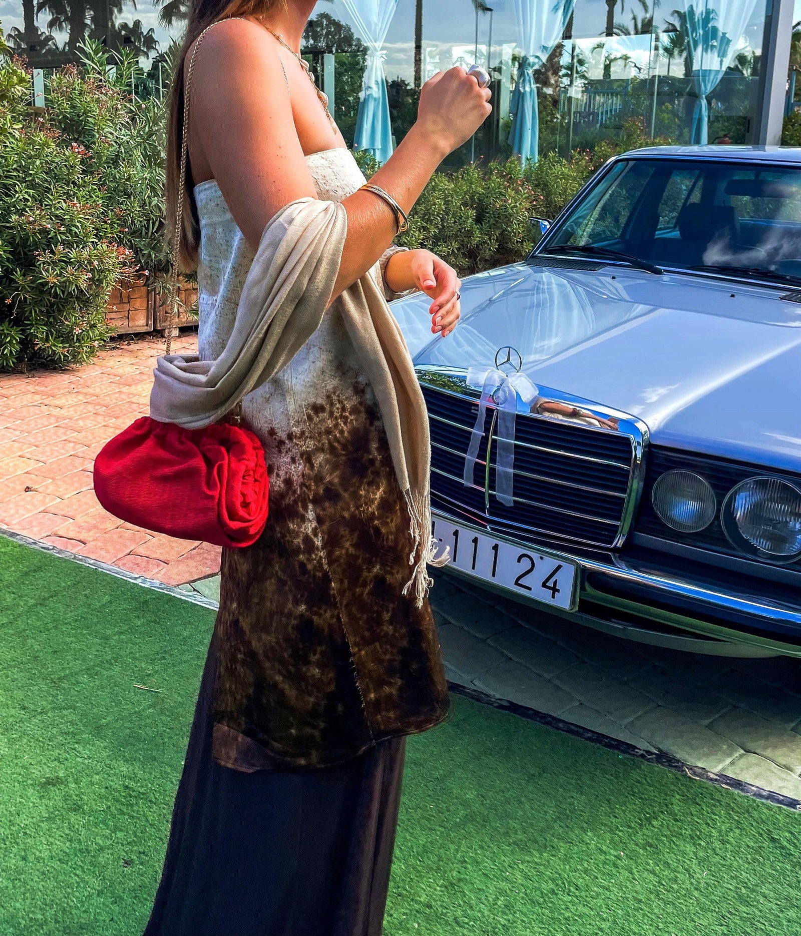 Woman holding a red purse with a leopard print bag over her shoulder, standing next to a classic Mercedes-Benz car.