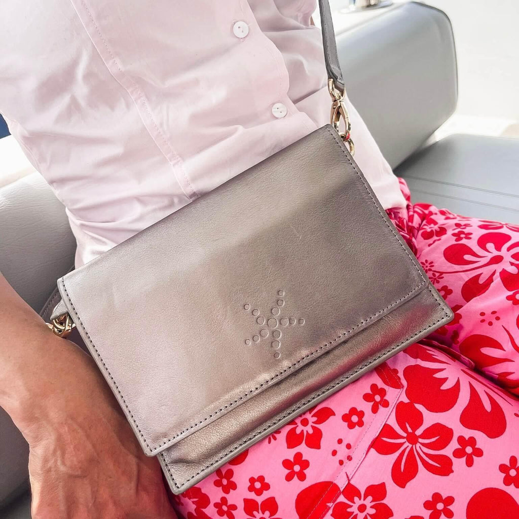 Person holding a silver clutch bag with a floral patterned bag and chair in the background