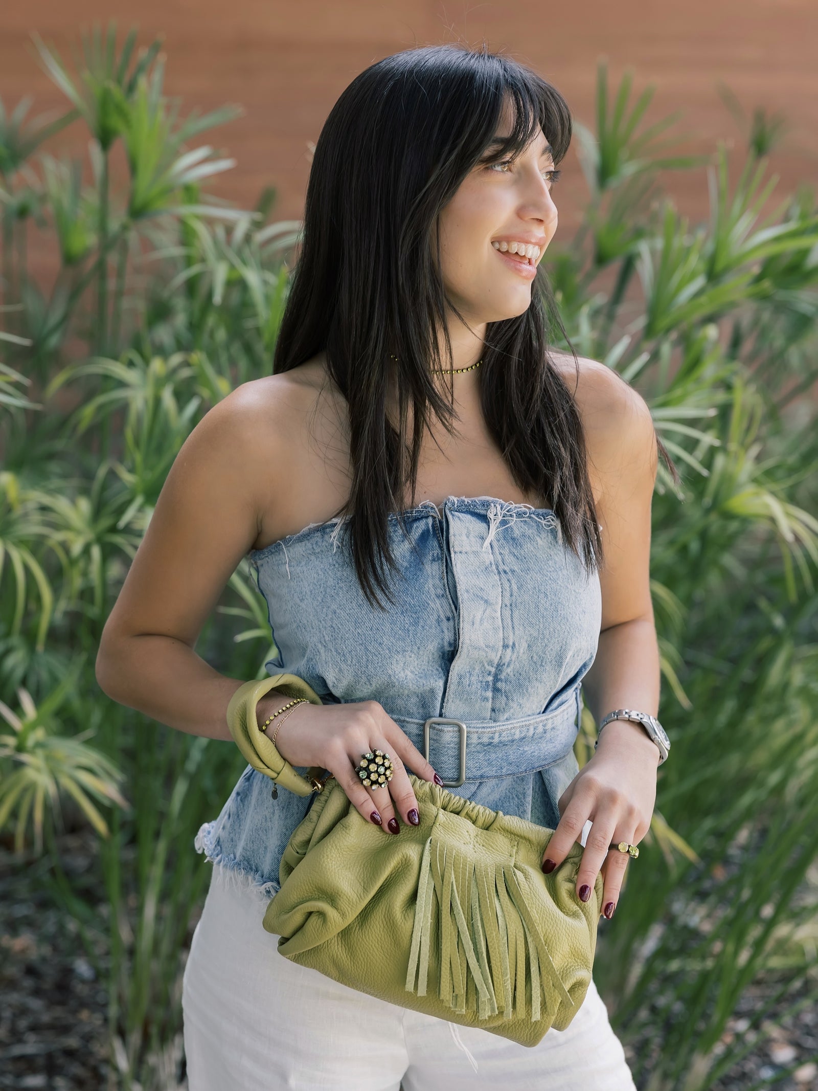 Woman holding a Natalia - Full Grain Leather Clutch Bag - Vinaigrette in front of green plants