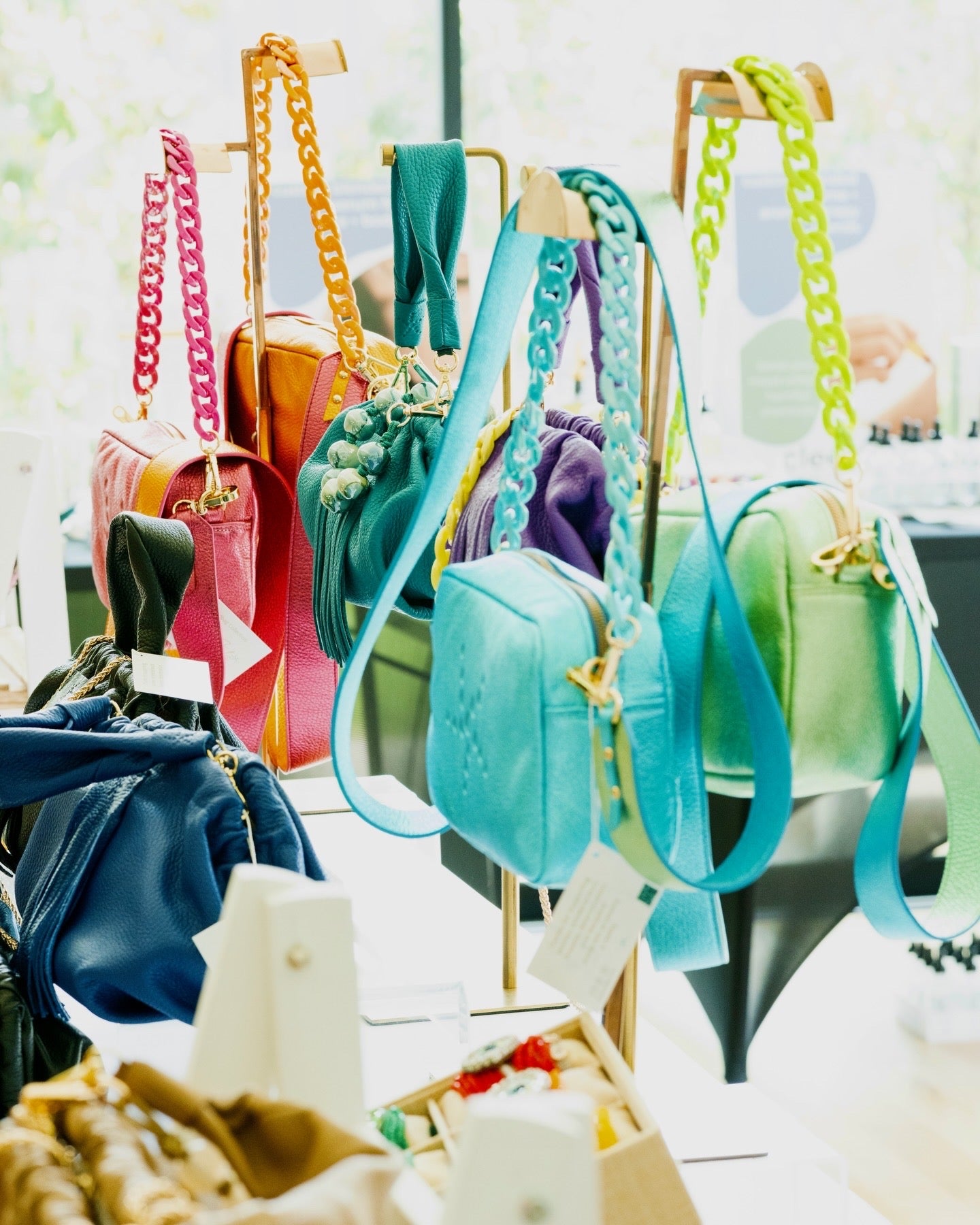 Colorful premium leather handbags displayed on stands with a blurred background