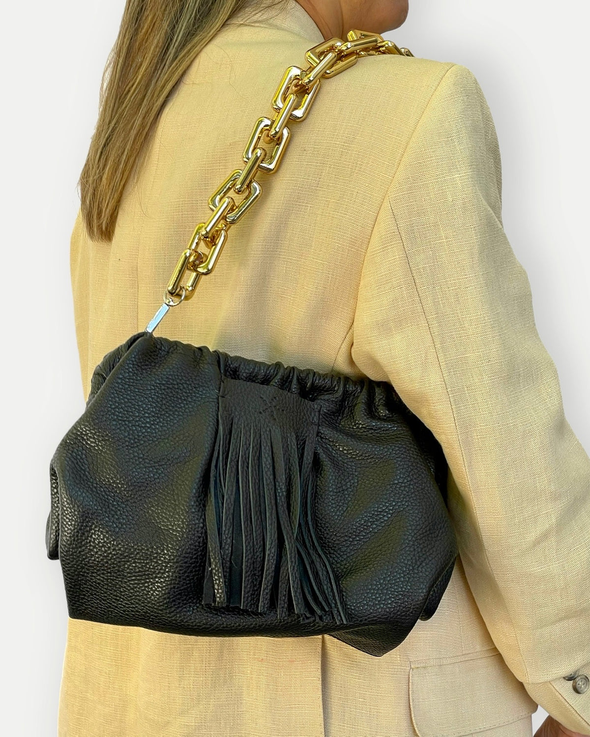 Black Natalia - Full Grain Leather Clutch  handbag with gold chain strap worn by a person in a beige outfit.