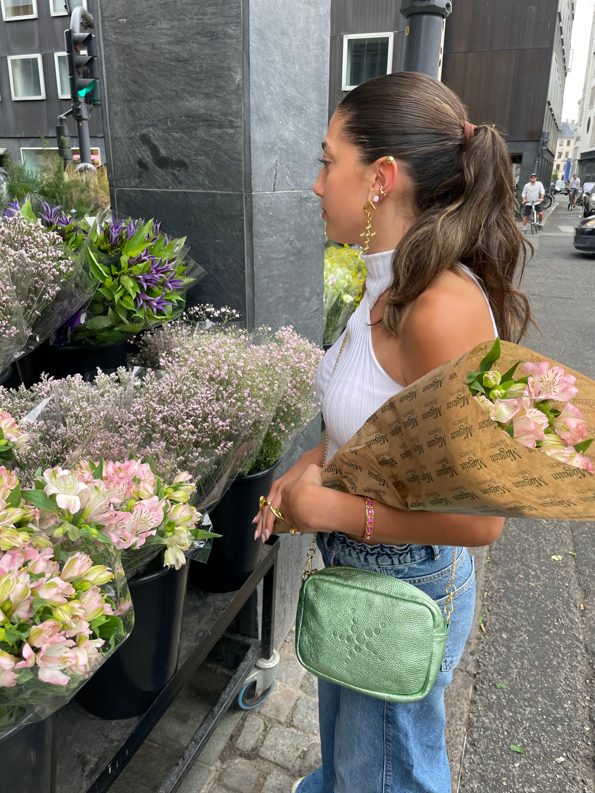 Woman holding a bouquet of flowers on a street, and Green Metallic Gabriela with flower stands in the background