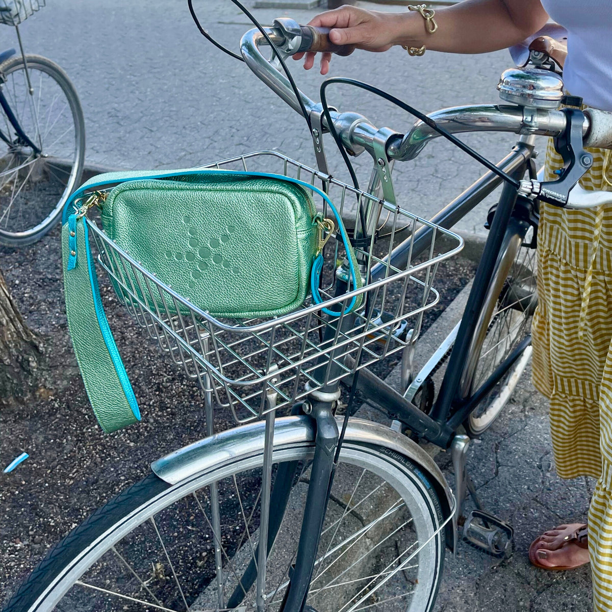 Green Metallic Grabriela handbag in a bicycle basket with a person partially visible