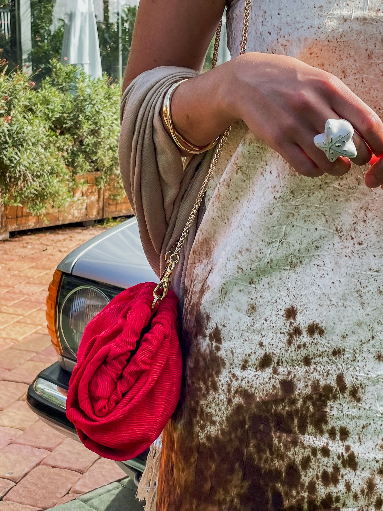 A  wedding guest wearing a red clutch with a gold chain, wearing a beige dress.